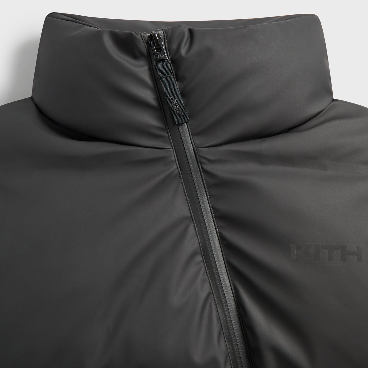 Close-up of the stand collar, asymmetric zip and tonal Kith logo on the black Filmore vest
